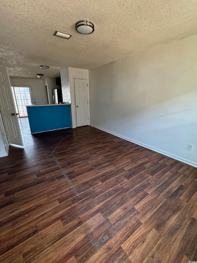 empty room featuring a textured ceiling, dark wood-type flooring, and baseboards