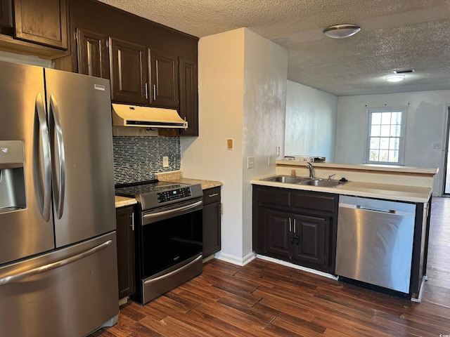 kitchen with appliances with stainless steel finishes, dark wood-style flooring, light countertops, under cabinet range hood, and a sink