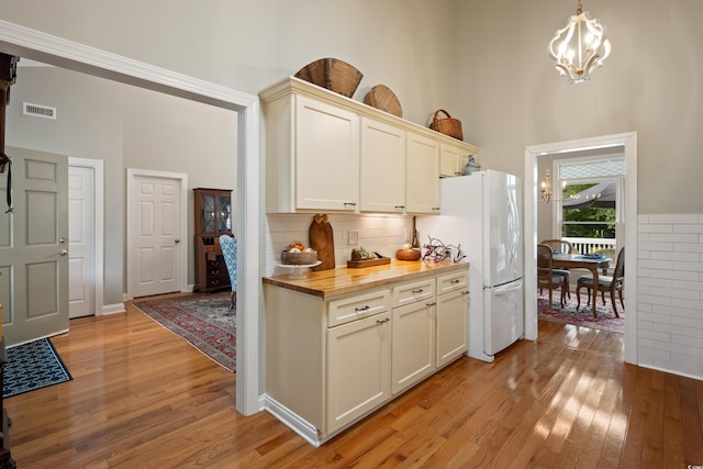 kitchen with light hardwood / wood-style flooring, wooden counters, decorative light fixtures, white fridge, and an inviting chandelier