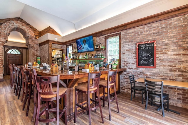 bar with vaulted ceiling, hardwood / wood-style floors, and brick wall