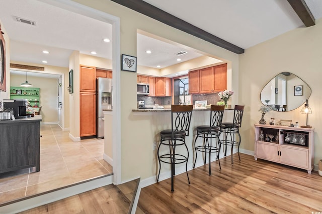 kitchen with appliances with stainless steel finishes, beamed ceiling, kitchen peninsula, a breakfast bar area, and tasteful backsplash