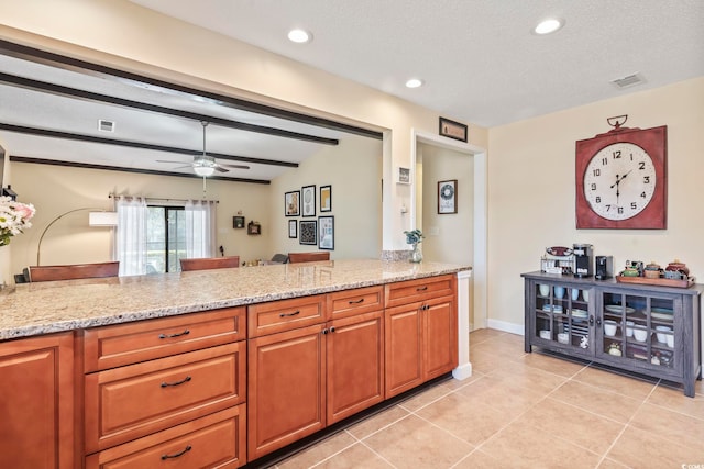 kitchen featuring kitchen peninsula, light stone countertops, ceiling fan, light tile patterned floors, and a textured ceiling