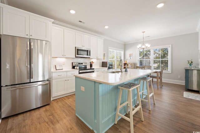 kitchen featuring appliances with stainless steel finishes, an island with sink, sink, white cabinets, and hanging light fixtures