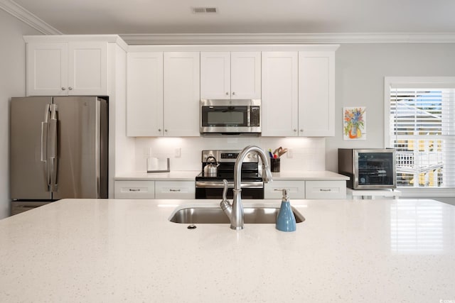 kitchen featuring white cabinetry, backsplash, stainless steel appliances, light stone counters, and ornamental molding