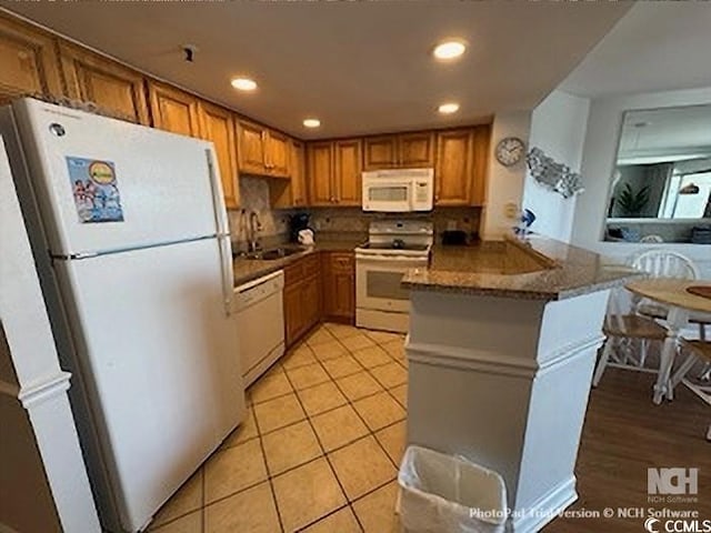 kitchen with white appliances, a peninsula, recessed lighting, a sink, and brown cabinets