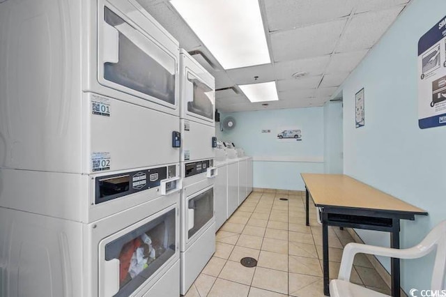 kitchen with white cabinetry, stacked washer and dryer, light tile patterned floors, and a drop ceiling