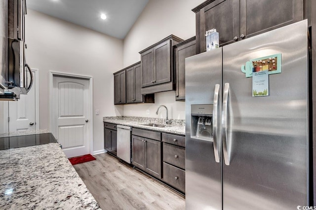 kitchen with sink, dark brown cabinets, appliances with stainless steel finishes, light stone countertops, and light hardwood / wood-style floors