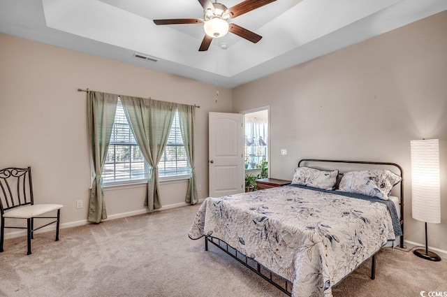 bedroom with light colored carpet, ceiling fan, and a tray ceiling