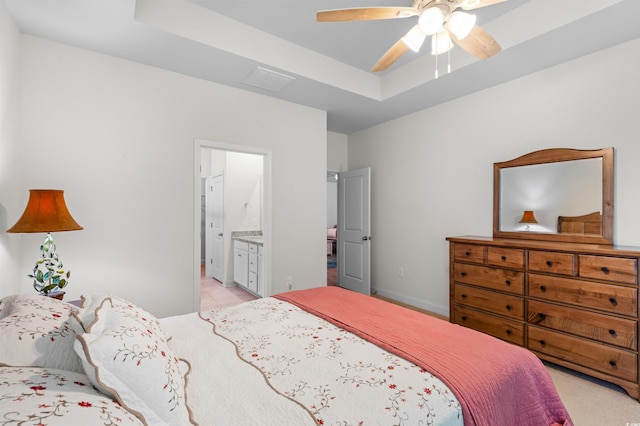 bedroom with light carpet, baseboards, a ceiling fan, ensuite bath, and a tray ceiling