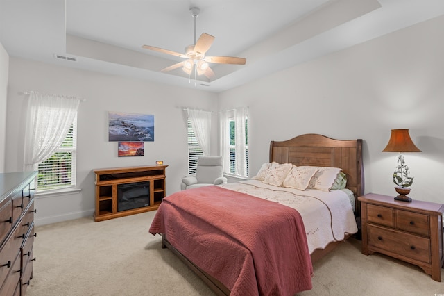 bedroom with multiple windows, visible vents, a raised ceiling, and light colored carpet