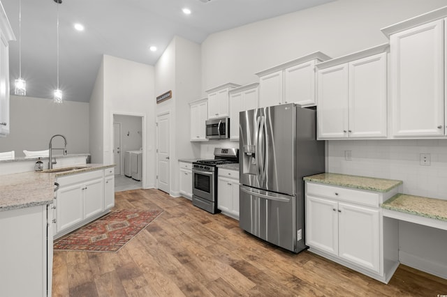 kitchen featuring a sink, white cabinetry, appliances with stainless steel finishes, light wood-type flooring, and washing machine and clothes dryer