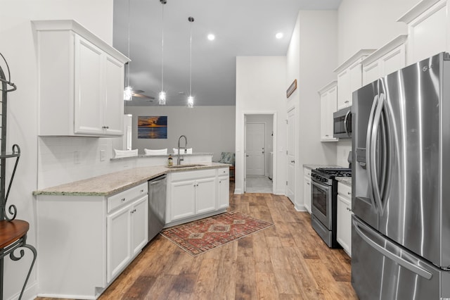 kitchen featuring a peninsula, a sink, white cabinetry, appliances with stainless steel finishes, and light wood-type flooring