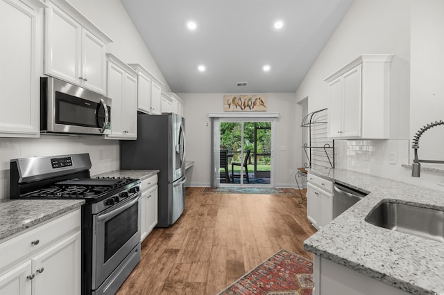 kitchen with lofted ceiling, light wood-style flooring, appliances with stainless steel finishes, white cabinetry, and a sink