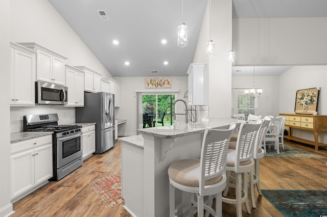 kitchen with light wood finished floors, white cabinets, a breakfast bar, a peninsula, and stainless steel appliances