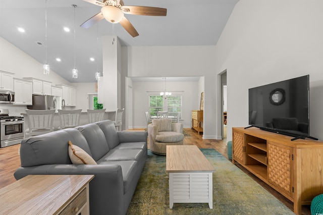 living room featuring high vaulted ceiling, ceiling fan with notable chandelier, wood finished floors, visible vents, and baseboards