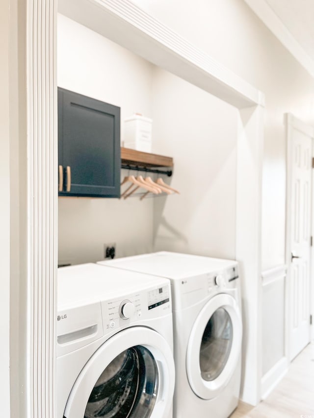 clothes washing area with laundry area, washing machine and dryer, and light wood-style floors