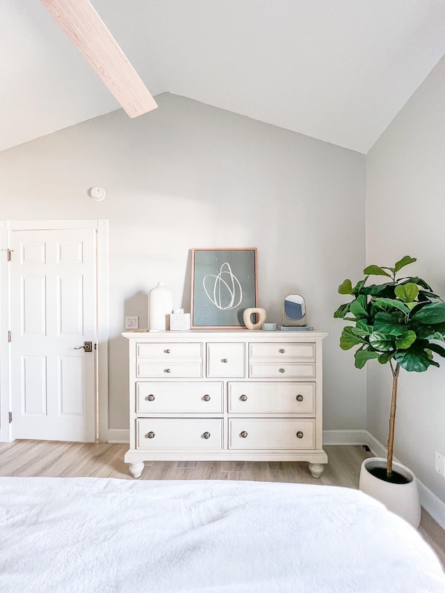 bedroom with lofted ceiling with beams, light wood-style flooring, and baseboards