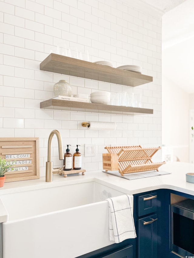 kitchen featuring open shelves, stainless steel microwave, blue cabinetry, and a sink