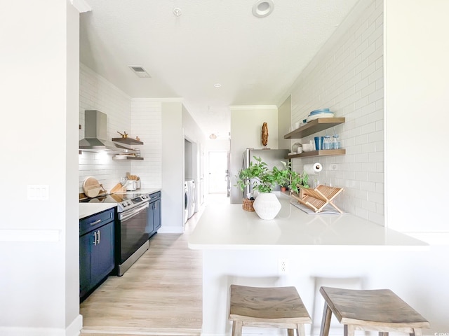 kitchen with stainless steel range with electric stovetop, wall chimney exhaust hood, blue cabinets, and open shelves