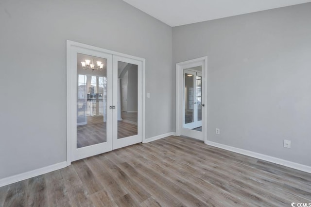 empty room with lofted ceiling, light hardwood / wood-style flooring, an inviting chandelier, and french doors