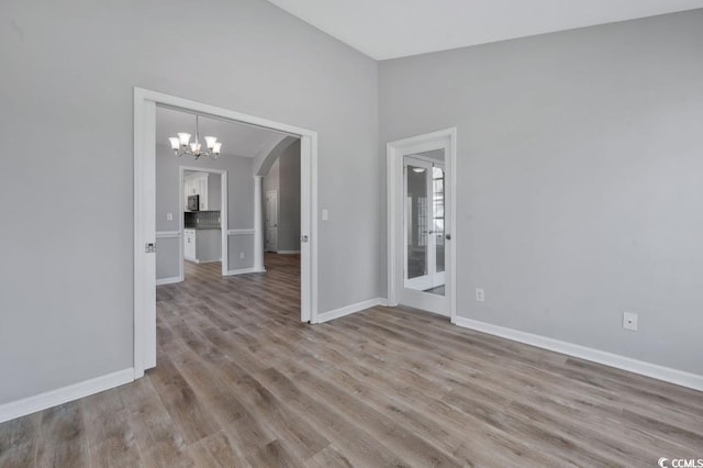 empty room featuring lofted ceiling, light hardwood / wood-style floors, and a chandelier