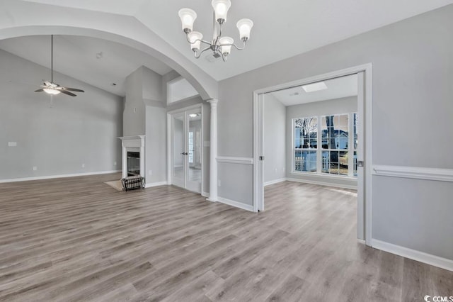 unfurnished living room with vaulted ceiling, ceiling fan with notable chandelier, and light hardwood / wood-style flooring