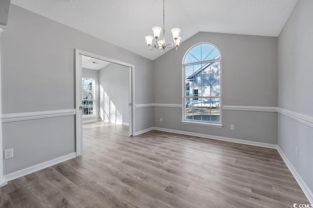 unfurnished dining area with an inviting chandelier, vaulted ceiling, and wood-type flooring