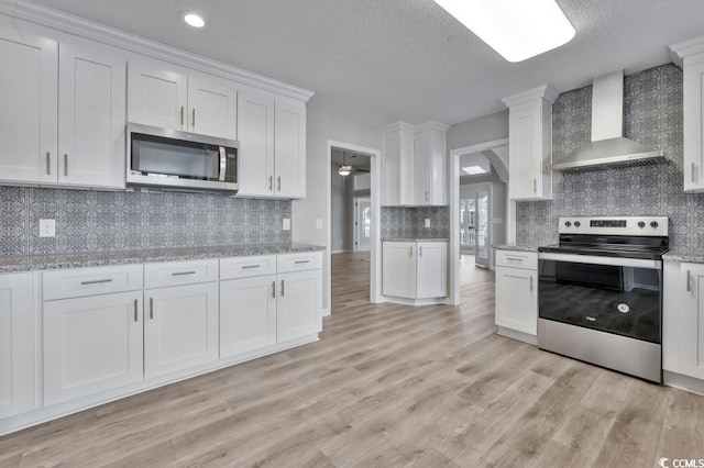 kitchen with white cabinets, light hardwood / wood-style floors, stainless steel appliances, light stone countertops, and wall chimney exhaust hood
