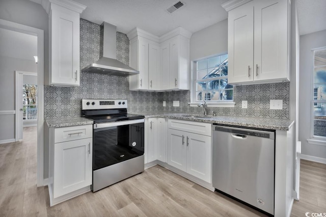 kitchen featuring sink, appliances with stainless steel finishes, white cabinetry, light stone countertops, and wall chimney exhaust hood