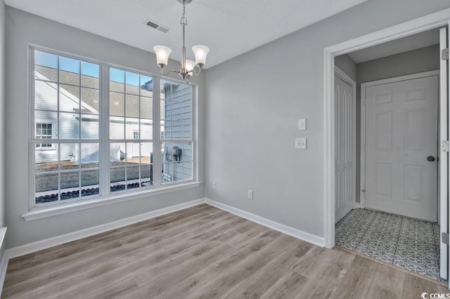 unfurnished dining area featuring an inviting chandelier and light hardwood / wood-style flooring
