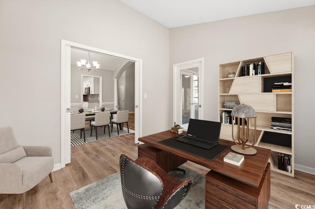 office space with an inviting chandelier, vaulted ceiling, and light hardwood / wood-style floors