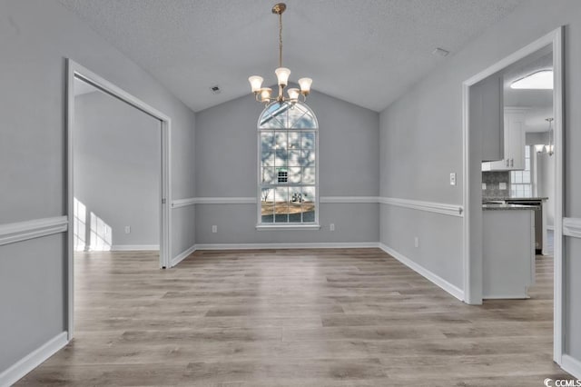 unfurnished dining area featuring lofted ceiling, a textured ceiling, an inviting chandelier, and light hardwood / wood-style flooring