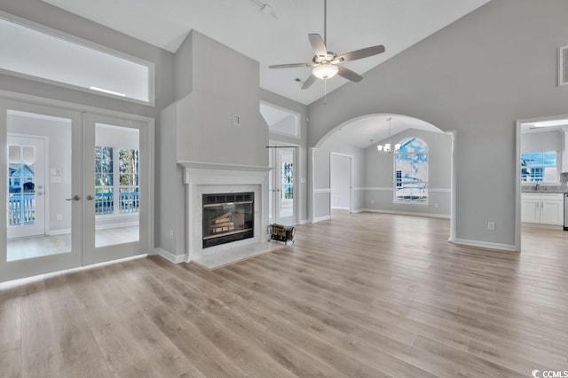 unfurnished living room featuring a fireplace, high vaulted ceiling, french doors, and light wood-type flooring