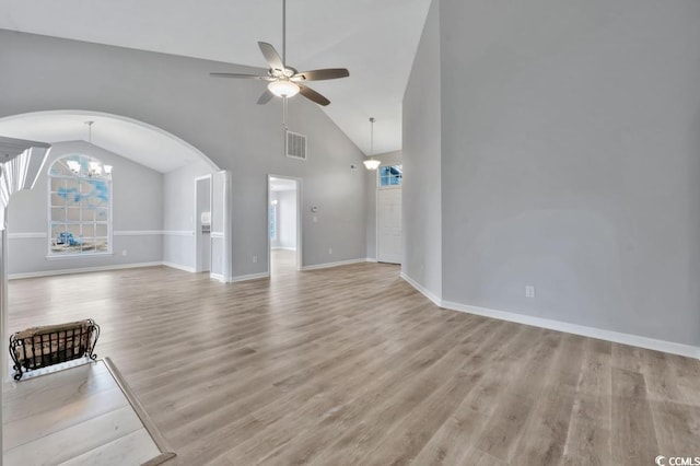 unfurnished living room featuring ceiling fan with notable chandelier, light hardwood / wood-style flooring, and high vaulted ceiling