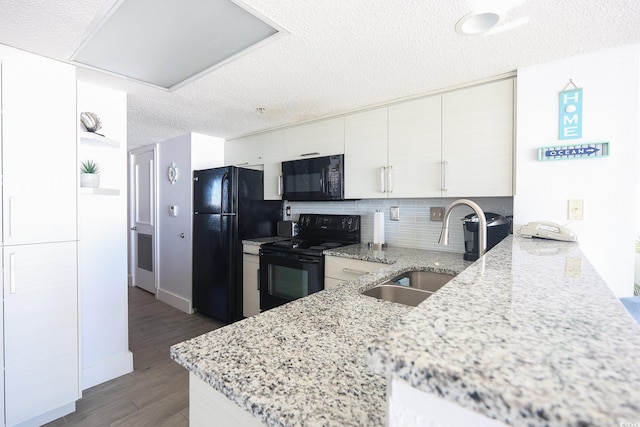 kitchen with sink, black appliances, light stone countertops, a textured ceiling, and kitchen peninsula