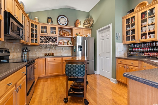 kitchen with appliances with stainless steel finishes, light hardwood / wood-style flooring, vaulted ceiling, and decorative backsplash