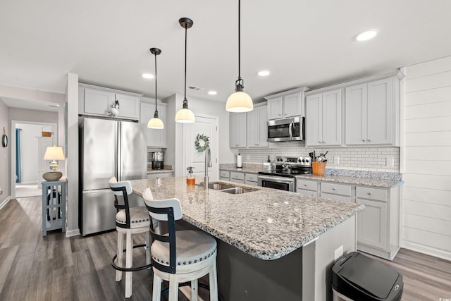 kitchen with appliances with stainless steel finishes, sink, hanging light fixtures, and a center island with sink