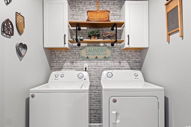 washroom with washing machine and clothes dryer, brick wall, and cabinets