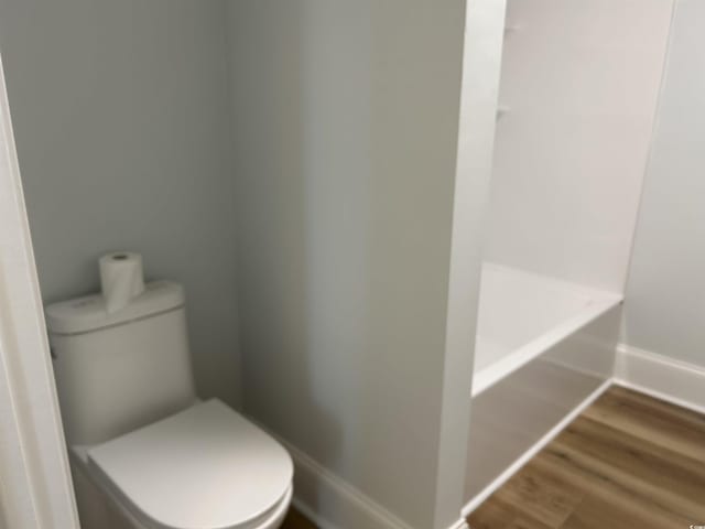 bathroom featuring toilet, a washtub, baseboards, and wood finished floors