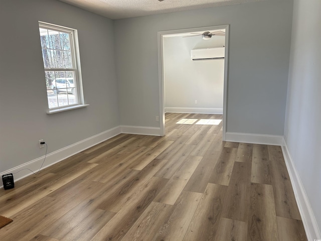 empty room with a wall mounted air conditioner, a textured ceiling, baseboards, and wood finished floors