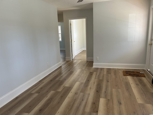 empty room with ceiling fan, a textured ceiling, baseboards, and wood finished floors