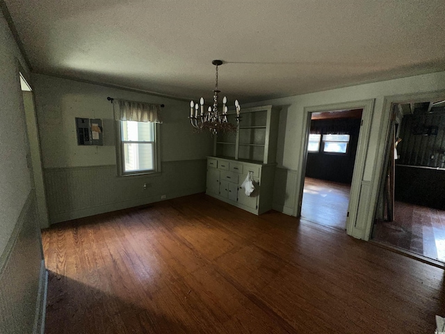 unfurnished dining area with dark hardwood / wood-style floors, a textured ceiling, electric panel, and an inviting chandelier