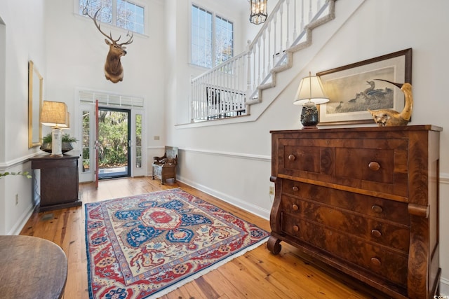 foyer entrance featuring light wood-type flooring, a chandelier, and a towering ceiling