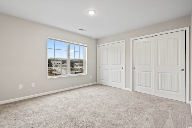 unfurnished bedroom with baseboards, visible vents, multiple closets, and carpet flooring