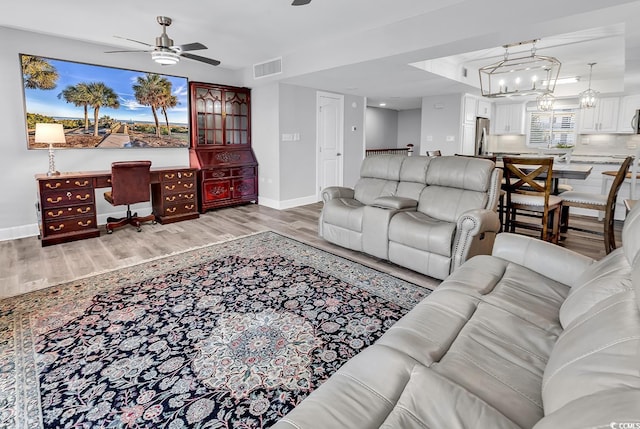 living room with light wood-type flooring and ceiling fan with notable chandelier