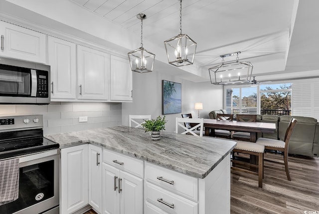 kitchen featuring wood-type flooring, backsplash, white cabinetry, stainless steel appliances, and hanging light fixtures