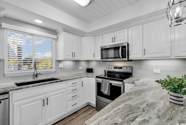 kitchen with appliances with stainless steel finishes, tasteful backsplash, hanging light fixtures, white cabinets, and sink