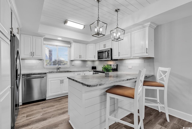 kitchen with a kitchen bar, sink, a tray ceiling, stainless steel appliances, and kitchen peninsula