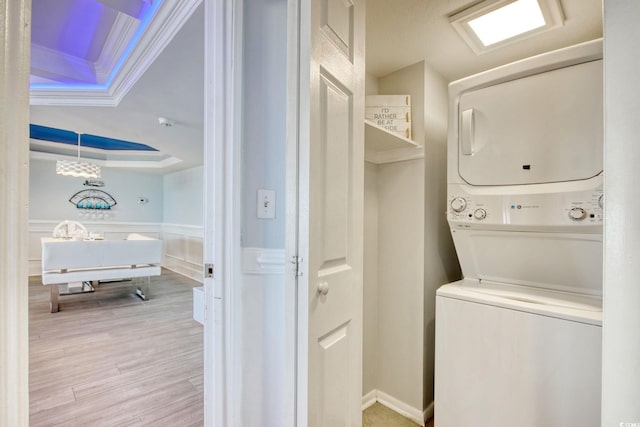 laundry area with crown molding, stacked washing maching and dryer, and light wood-type flooring