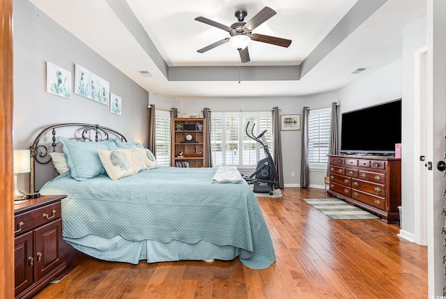 bedroom with hardwood / wood-style floors, ceiling fan, and a tray ceiling